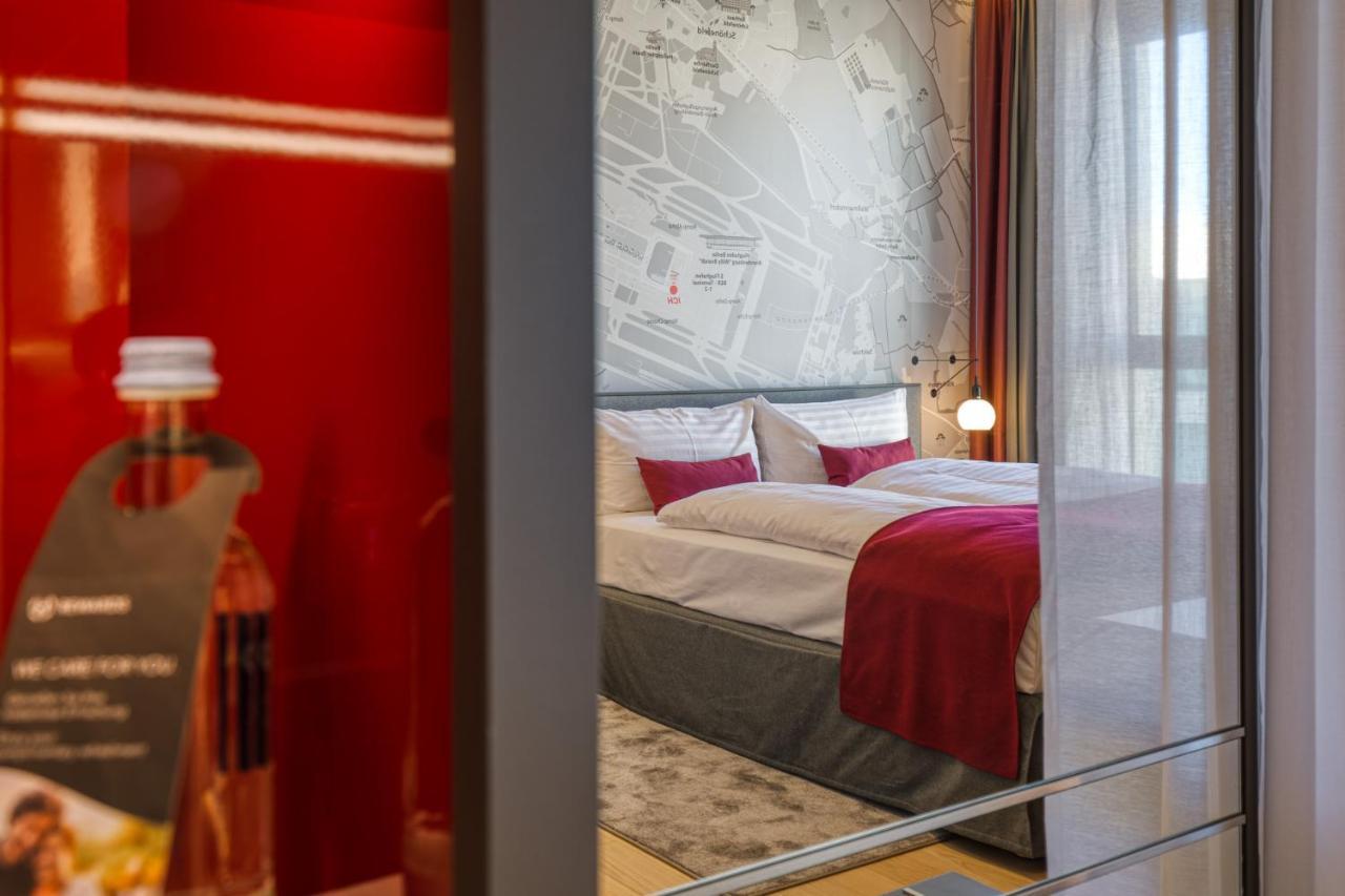 Intercityhotel Berlin Airport Ber Terminal 1 & 2 Schoenefeld Luaran gambar The photo shows a modern hotel room that features a comfortable bed with white linens and a red accent blanket. Behind the bed is a stylish wall displaying a map design. The room has large windows dressed with light-colored curtains, allowing natural