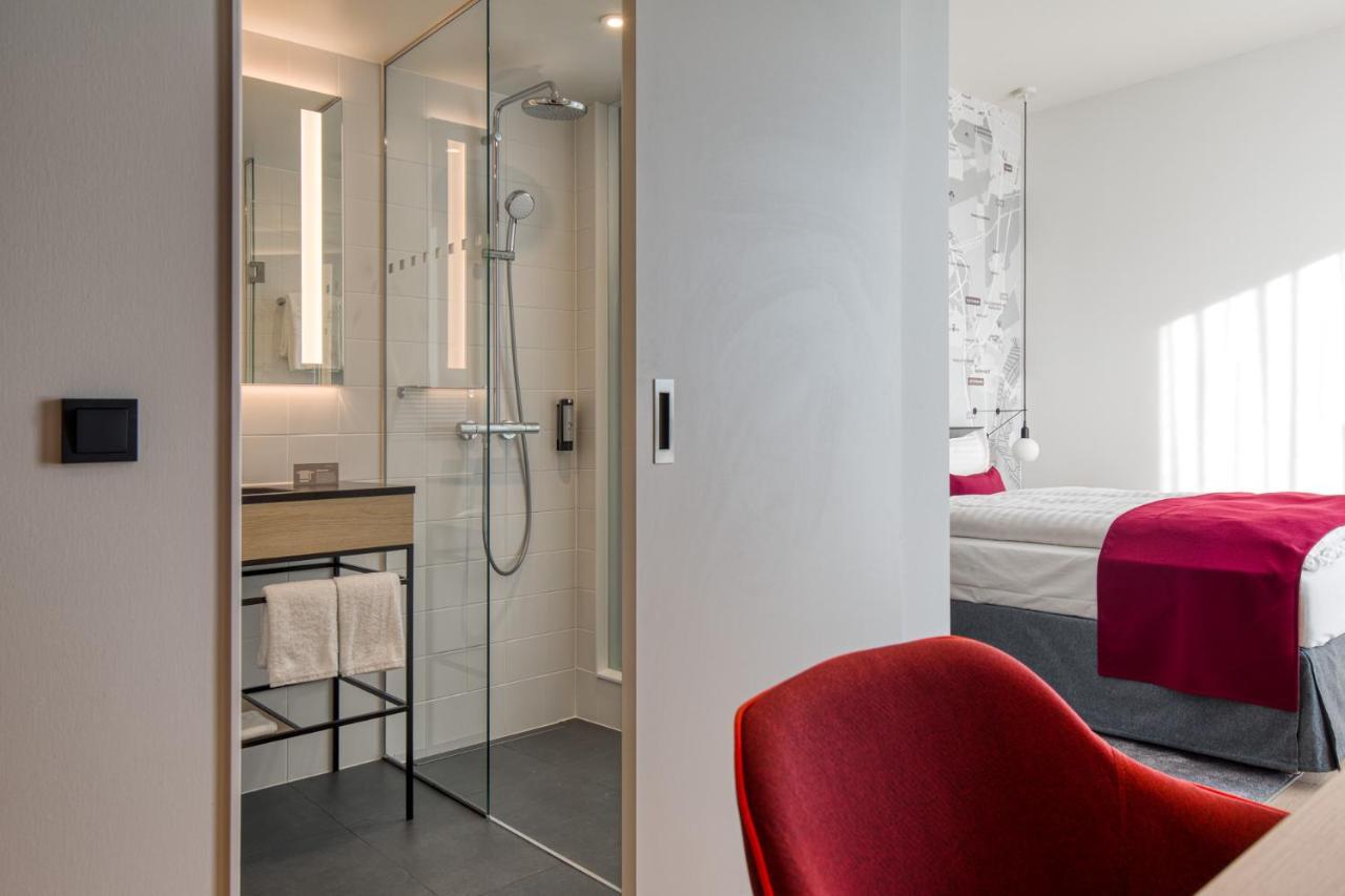 Intercityhotel Berlin Airport Ber Terminal 1 & 2 Schoenefeld Luaran gambar The photo shows a modern hotel room or bathroom space. On the left, there is a glass-enclosed shower area with a sleek design, featuring a showerhead and minimalist fixtures. Adjacent to the shower, there's a sink area with a stylish countertop and a